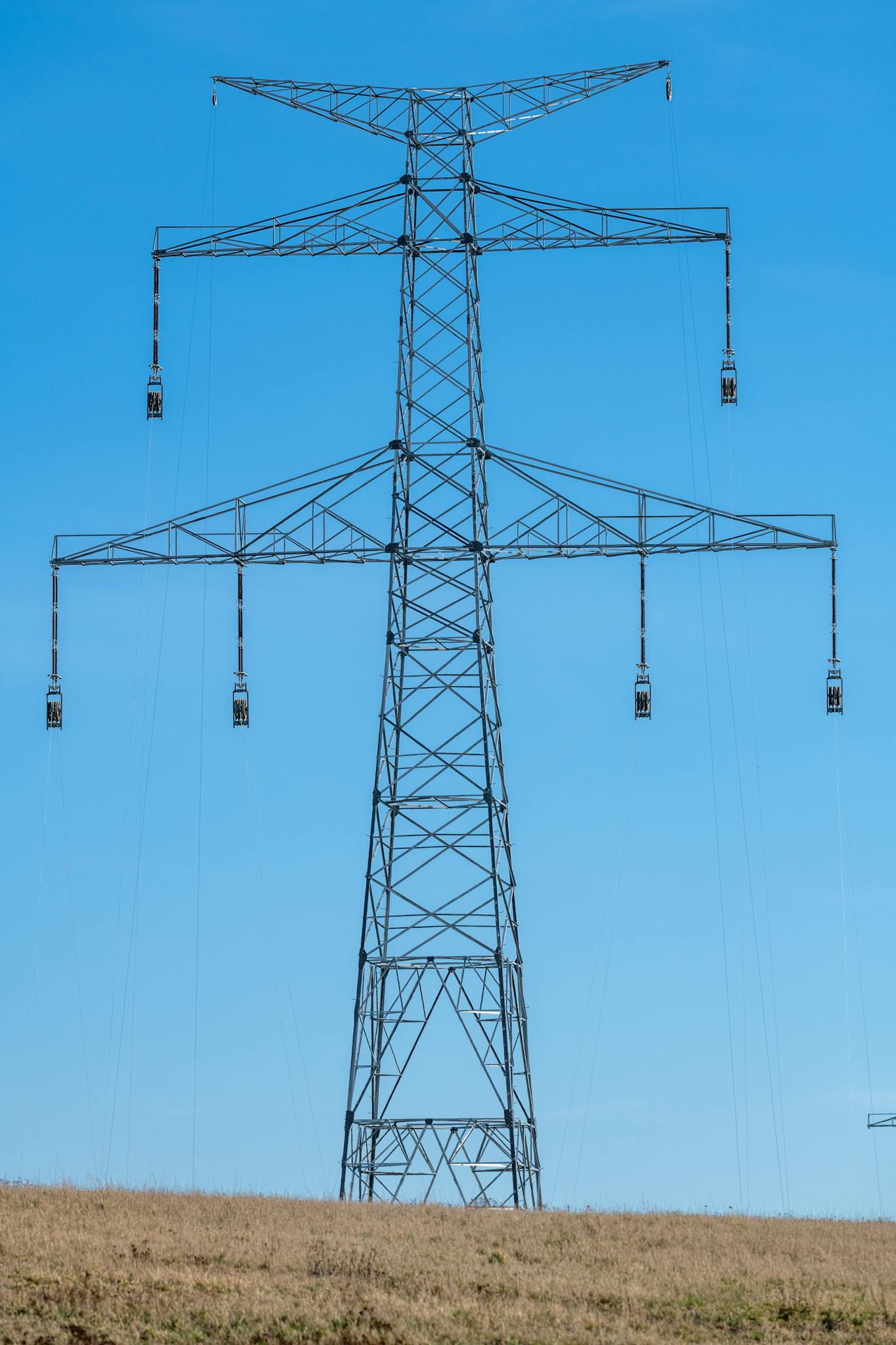 A towering electricity pylon standing prominently in a vast open field under a clear blue sky.