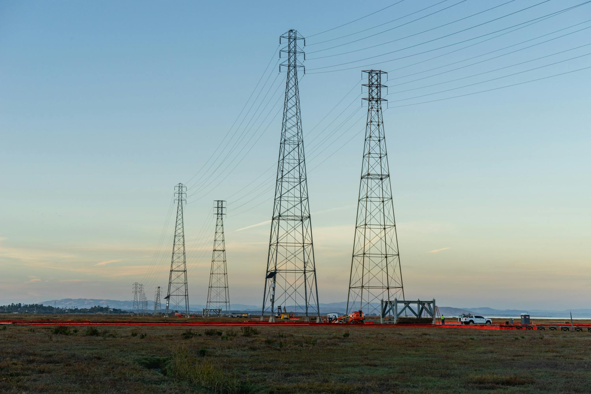 High voltage transmission towers with clear blue sky at dusk in an open field.