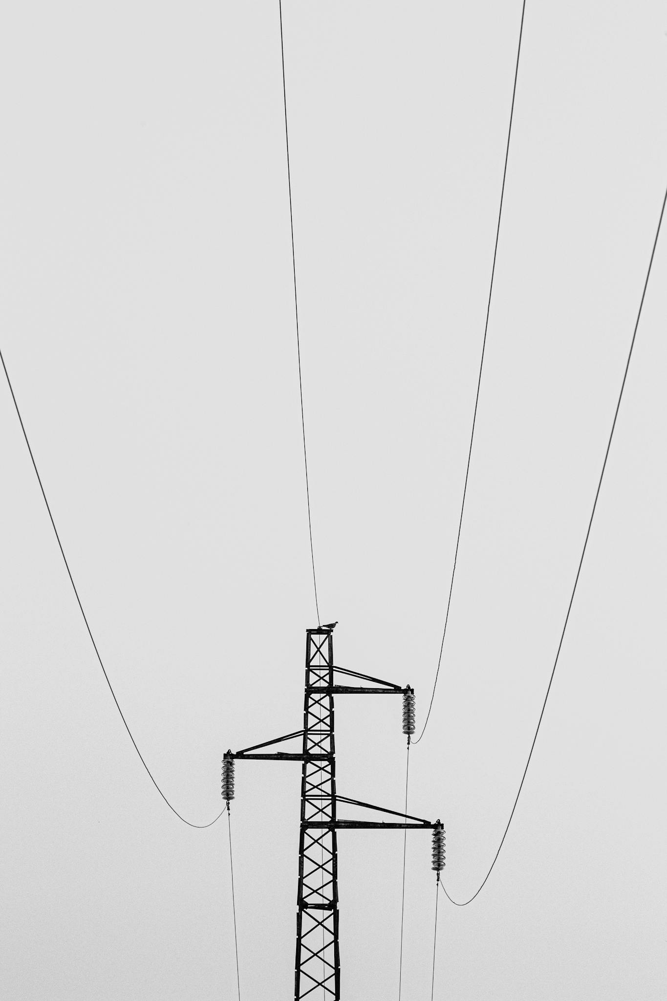 Minimalistic view of a high voltage transmission tower against a cloudy sky.